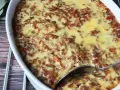 LCHF moussaka i ugnsform, gyllene och bubblande. En sked är redo att servera denna läckra, köttfärsfyllda gratäng.