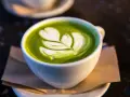 En vit kopp med grön matcha latte, dekorerad med mjölkskum. Även om det är gott, kan man uppleva matcha te biverkningar om man dricker för mycket.