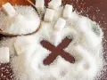 Socker i en sked och utspritt på en mörk yta, med en "X" formad ur sockret. Dags att rensa magen från socker!