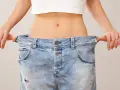 En person visar upp sina jeans som är alldeles för stora, ett tydligt tecken på att hon lyckats gå ner 10 kg.