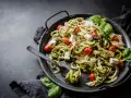 En läcker keto middag med kyckling, zucchinipasta, körsbärstomater och fetaost, garnerad med färsk basilika.