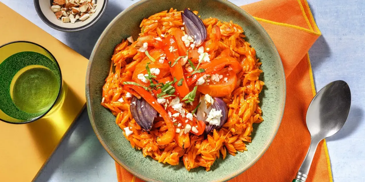 En skål med orzopasta med rostade grönsaker och fetaost, ett härligt medelhavskost recept. Toppad med mandlar och färska örter.