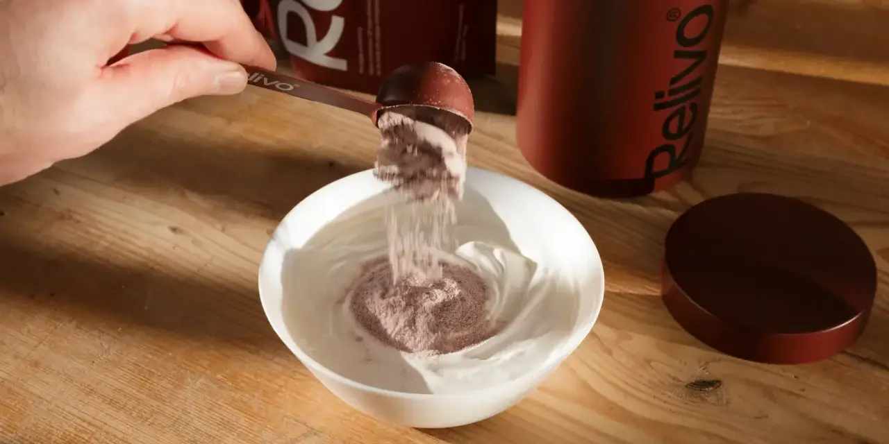 Pulver från en skopa blandas i en skål med yoghurt. En burk och förpackning från Relivo syns i bakgrunden. Perfekt för att dricka mer!