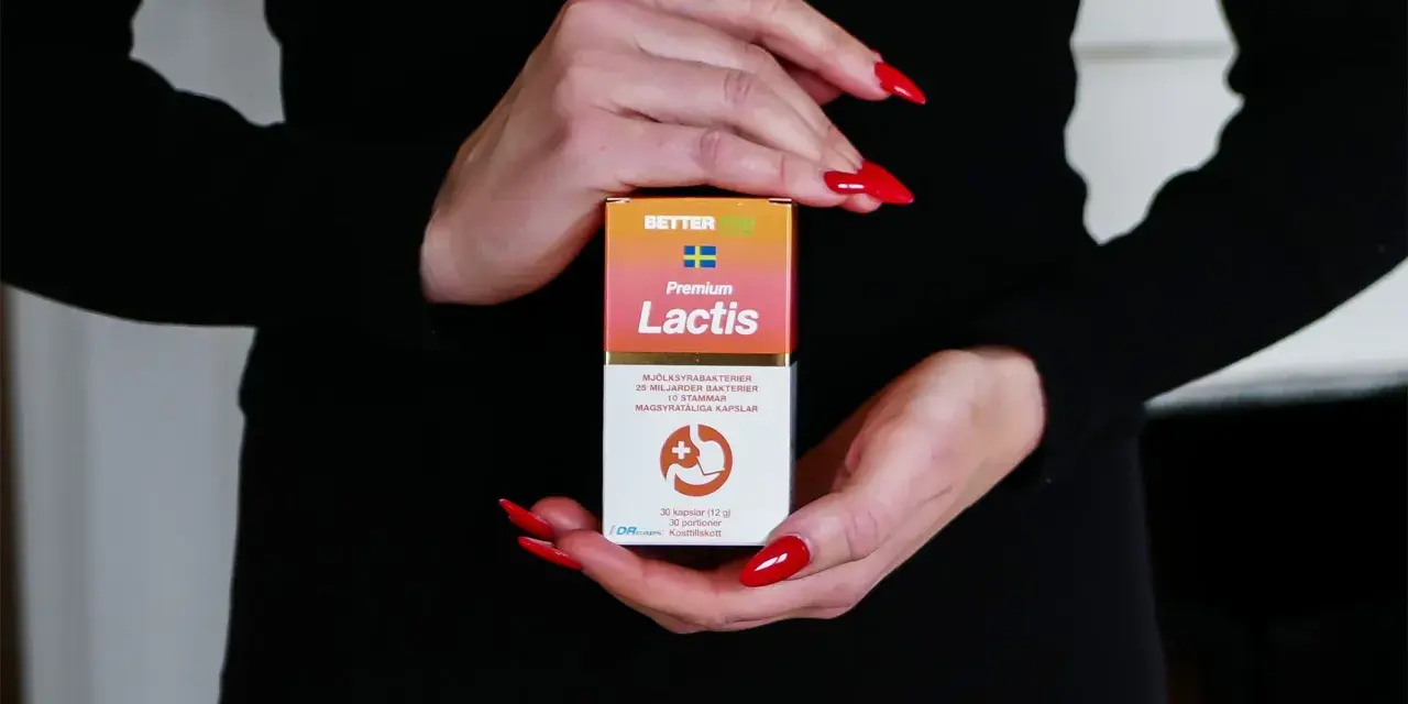 Händer med röda naglar håller en kartong med probiotika för IBS. Lactis innehåller mjölksyrabakterier för magen.