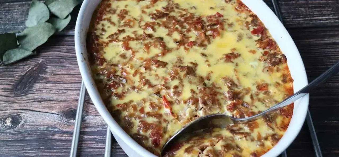 LCHF moussaka i ugnsform, gyllene och bubblande. En sked är redo att servera denna läckra, köttfärsfyllda gratäng.