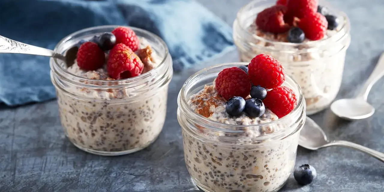 Tre burkar med overnight oats recept, toppade med hallon och blåbär. En perfekt frukost att förbereda kvällen innan.