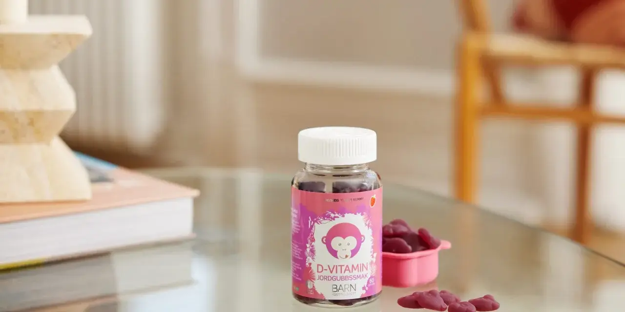 D-vitamin jordgubbssmak för barn. En burk med rosa etikett och en apa, bredvid en rosa skål med hjärtformade gummies.