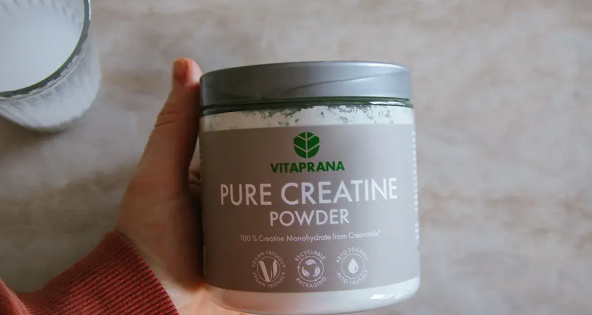 En hand håller en burk med VitaPrana Pure Creatine Powder. Kan vara ett bra tillskott för att hantera energi under klimakteriet.