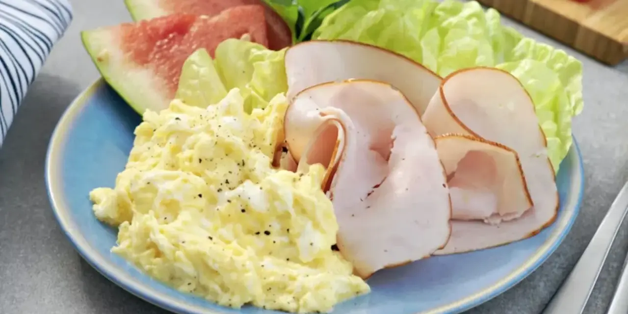 En blå tallrik med äggröra, kalkonpålägg, vattenmelon och sallad. En perfekt 5:2 frukost för en hälsosam start.