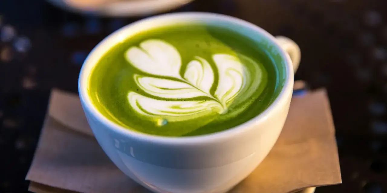 En vit kopp med grön matcha latte, dekorerad med mjölkskum. Även om det är gott, kan man uppleva matcha te biverkningar om man dricker för mycket.