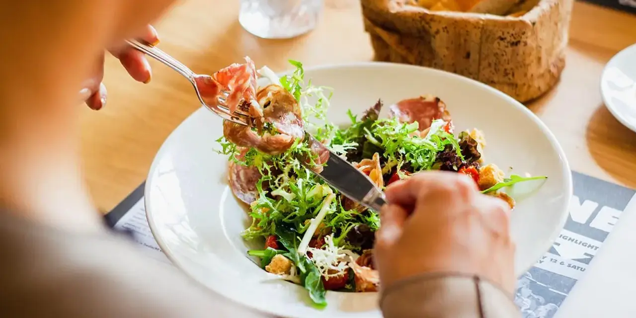 En person äter en sallad med skinka, en del av en 800 kcal diet. Brödkorg i bakgrunden.