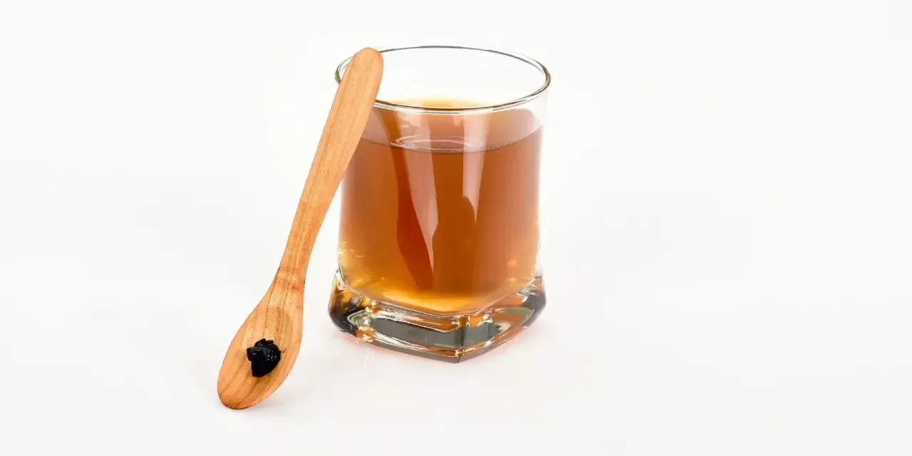En träsked med shilajit bredvid ett glas med en brun dryck. Var medveten om potentiella shilajit biverkningar.