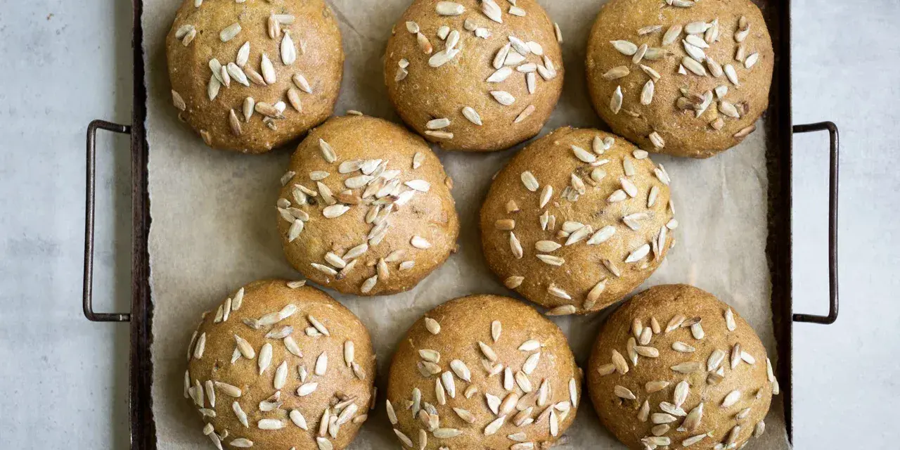 Nio gyllene glutenfria morotsfrallor toppade med solrosfrön ligger på en plåt.