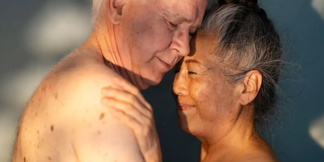 Ett äldre par omfamnar varandra ömt, deras ansikten nära varandra. Ljuset faller mjukt över dem och framhäver deras hud. Kärlek och närhet lyser igenom, en påminnelse om att bra sex kan finnas i alla åldrar.