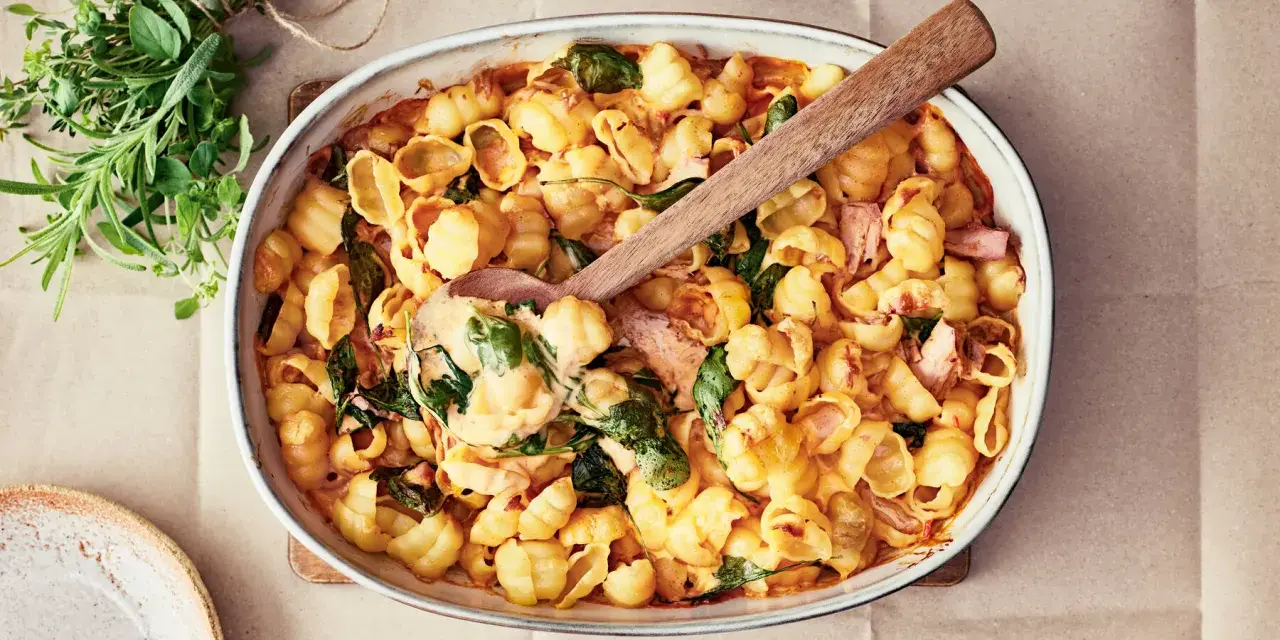 En krämig pastarätt med spenat och lax, perfekt för nyttiga recept. En träsked lyfter upp en portion ur ugnsformen.