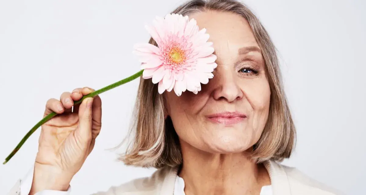 En kvinna med en rosa blomma framför ögat. Hon ler mjukt, en symbol för att hon mår bra och kanske vill gå ner i vikt under klimakteriet.