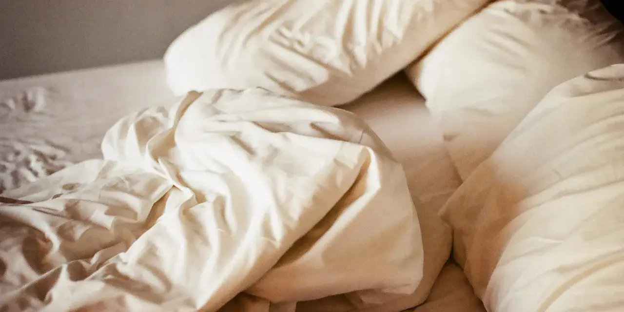 Ovanpå en bädd med vita lakan och kuddar, en påminnelse om att sömnmedel som melatonin kan ge biverkningar.