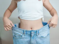 En person visar upp sina för stora jeans, ett tydligt tecken på att de lyckats gå ner i vikt.