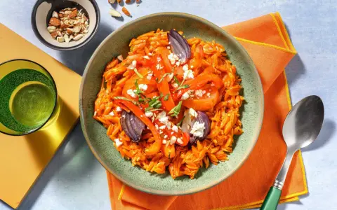 En skål med orzopasta med rostade grönsaker och fetaost, ett härligt medelhavskost recept. Toppad med mandlar och färska örter.