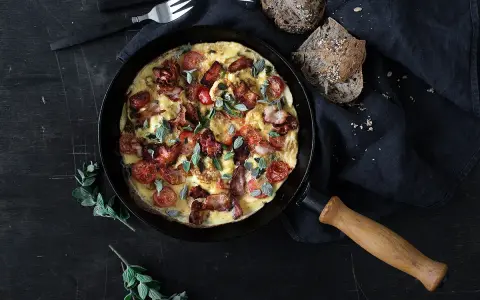 En saftig omelett med knaprigt bacon och körsbärstomater, serverad i en gjutjärnsstekpanna. Perfekt för en härlig frukost eller brunch.