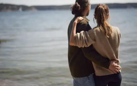 Par vid vattnet, en kvinna i sin bästa ålder med sexlust, omfamnar sin partner.
