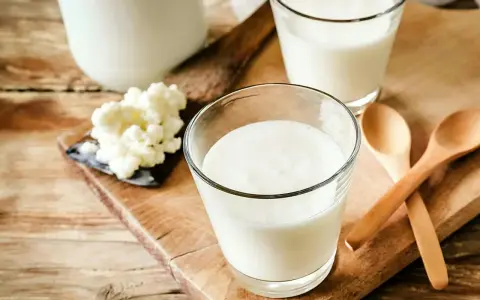 Två glas med krämig kefir står på en träskärbräda. Bredvid syns kefir-kultur och två träskedar. Kefir nyttigt för magen!