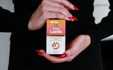 Händer med röda naglar håller en kartong med probiotika för IBS. Lactis innehåller mjölksyrabakterier för magen.