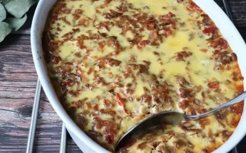 LCHF moussaka i ugnsform, gyllene och bubblande. En sked är redo att servera denna läckra, köttfärsfyllda gratäng.