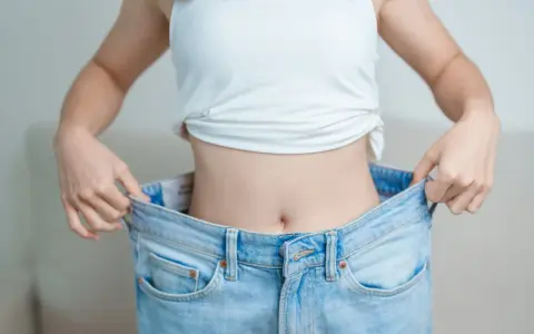 En person visar upp sina för stora jeans, ett tydligt tecken på att de lyckats gå ner i vikt.