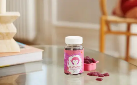 D-vitamin jordgubbssmak för barn. En burk med rosa etikett och en apa, bredvid en rosa skål med hjärtformade gummies.