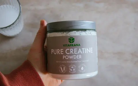 En hand håller en burk med VitaPrana Pure Creatine Powder. Kan vara ett bra tillskott för att hantera energi under klimakteriet.