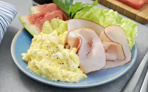 En blå tallrik med äggröra, kalkonpålägg, vattenmelon och sallad. En perfekt 5:2 frukost för en hälsosam start.
