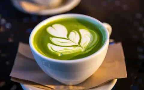 En vit kopp med grön matcha latte, dekorerad med mjölkskum. Även om det är gott, kan man uppleva matcha te biverkningar om man dricker för mycket.