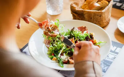 En person äter en sallad med skinka, en del av en 800 kcal diet. Brödkorg i bakgrunden.