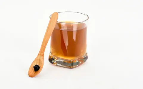 En träsked med shilajit bredvid ett glas med en brun dryck. Var medveten om potentiella shilajit biverkningar.