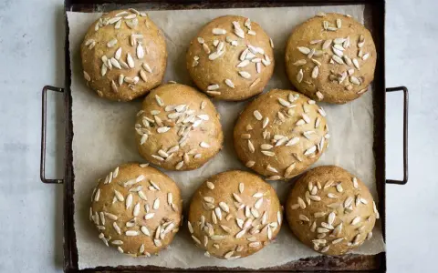 Nio gyllene glutenfria morotsfrallor toppade med solrosfrön ligger på en plåt.