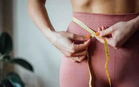 En person mäter midjan med ett måttband. Frågan "hur mycket kan man gå ner i vikt med Ozempic?" är relevant för många som vill förändra sin kropp.