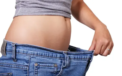En person visar hur stora jeansen blivit efter viktnedgång. Ibland är det svårt att gå ner i vikt hormoner kan spela roll.