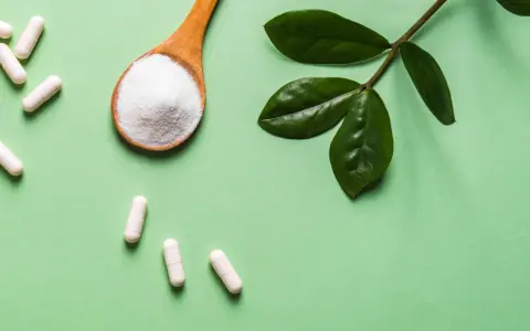 Vita kapslar och en sked med vitt pulver, bredvid gröna blad. Information om moringa biverkningar kan vara relevant.