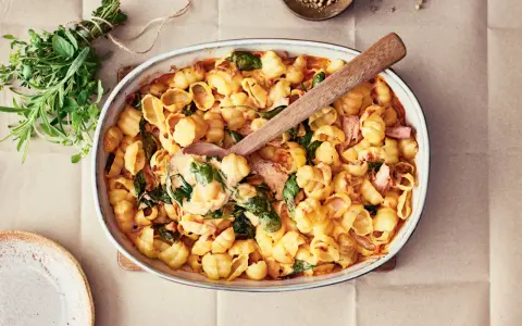 En krämig pastarätt med spenat och lax, perfekt för nyttiga recept. En träsked lyfter upp en portion ur ugnsformen.