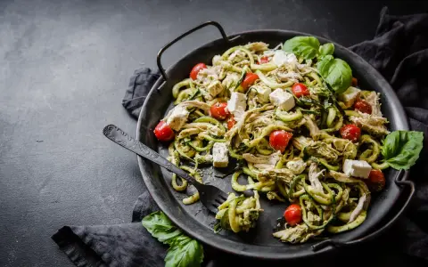 En läcker keto middag med kyckling, zucchinipasta, körsbärstomater och fetaost, garnerad med färsk basilika.