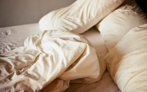 Ovanpå en bädd med vita lakan och kuddar, en påminnelse om att sömnmedel som melatonin kan ge biverkningar.