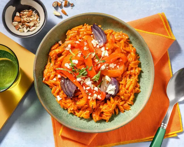 En skål med orzopasta med rostade grönsaker och fetaost, ett härligt medelhavskost recept. Toppad med mandlar och färska örter.