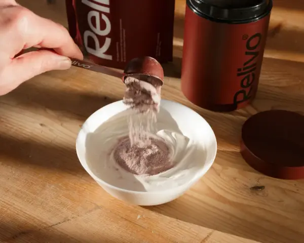 Pulver från en skopa blandas i en skål med yoghurt. En burk och förpackning från Relivo syns i bakgrunden. Perfekt för att dricka mer!