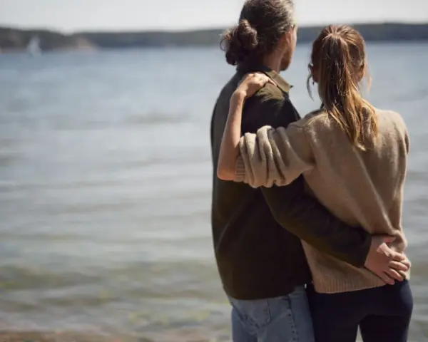 Par vid vattnet, en kvinna i sin bästa ålder med sexlust, omfamnar sin partner.