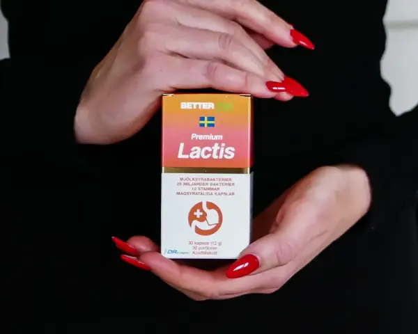 Händer med röda naglar håller en kartong med probiotika för IBS. Lactis innehåller mjölksyrabakterier för magen.
