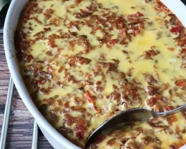 LCHF moussaka i ugnsform, gyllene och bubblande. En sked är redo att servera denna läckra, köttfärsfyllda gratäng.