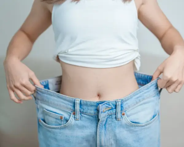 En person visar upp sina för stora jeans, ett tydligt tecken på att de lyckats gå ner i vikt.