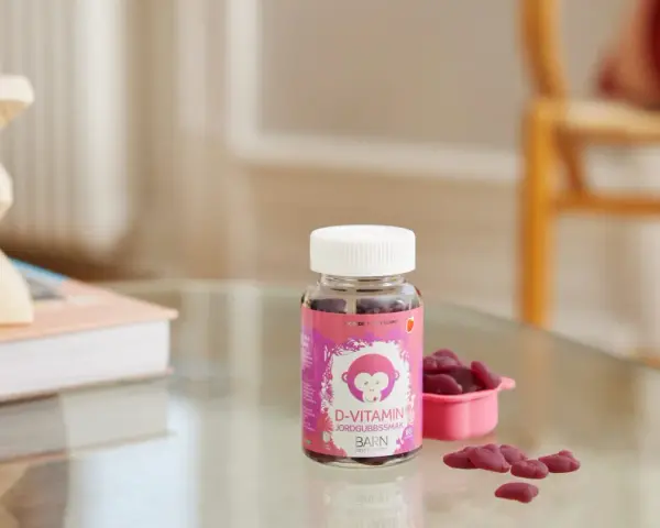 D-vitamin jordgubbssmak för barn. En burk med rosa etikett och en apa, bredvid en rosa skål med hjärtformade gummies.