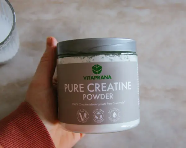 En hand håller en burk med VitaPrana Pure Creatine Powder. Kan vara ett bra tillskott för att hantera energi under klimakteriet.